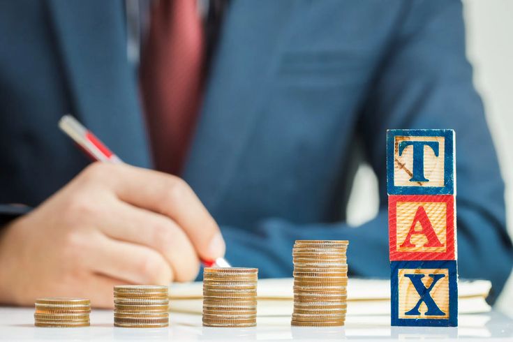 Who Is Taxable Person Under GST 1 "Businessman writing with tax-related concept, stacks of coins and tax blocks representing financial planning and tax management."